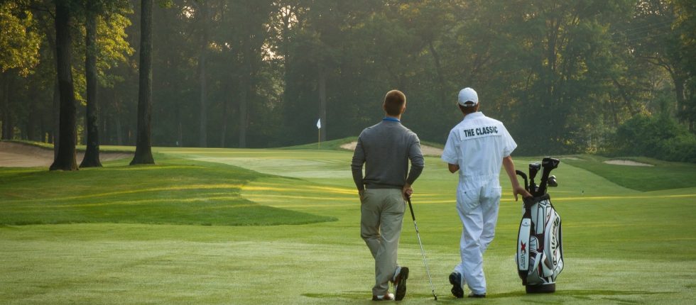 Golfer and his caddy at Maddens leaning on golf club admiring the Classic Golf course