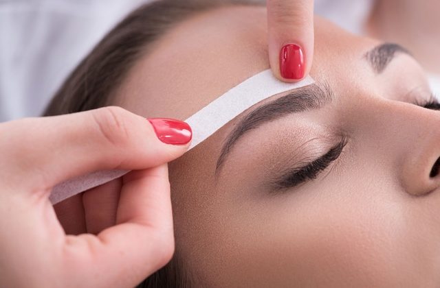 A therapist's hand waxing a woman's eyebrows