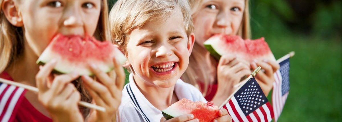 Children eating watermelon slices while holding their miniature American flags.