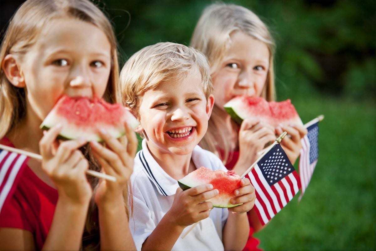 Children eating watermelon slices while holding their miniature American flags.