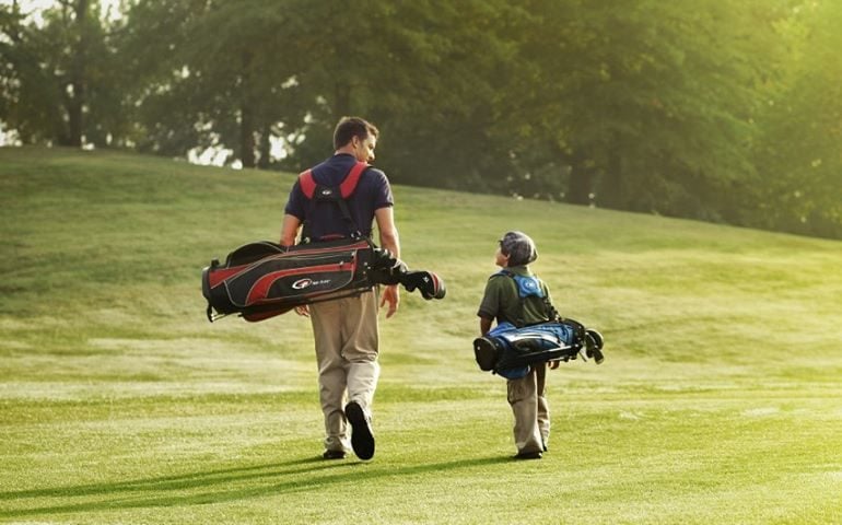 Father and Son walk on golf course with golf clubs slung over their shoulders