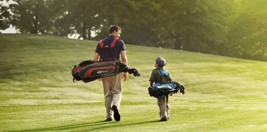 Father and Son walk on golf course with golf clubs slung over their shoulders