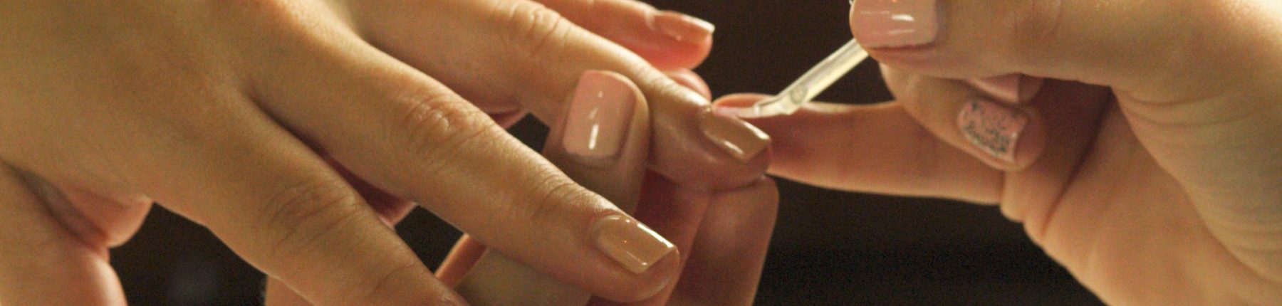 aesthetician's hand applying nail polish to the client's nails