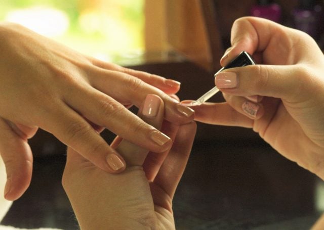 aesthetician's hand applying nail polish to the client's nails