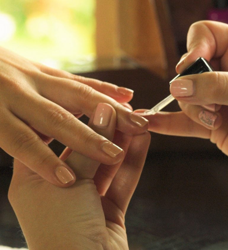 aesthetician's hand applying nail polish to the client's nails