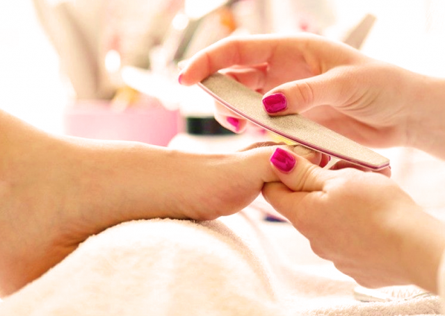 aesthetican's hands buffing the guest's toenails