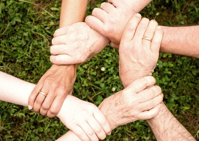 All hands holding the wrists in the outdoors.