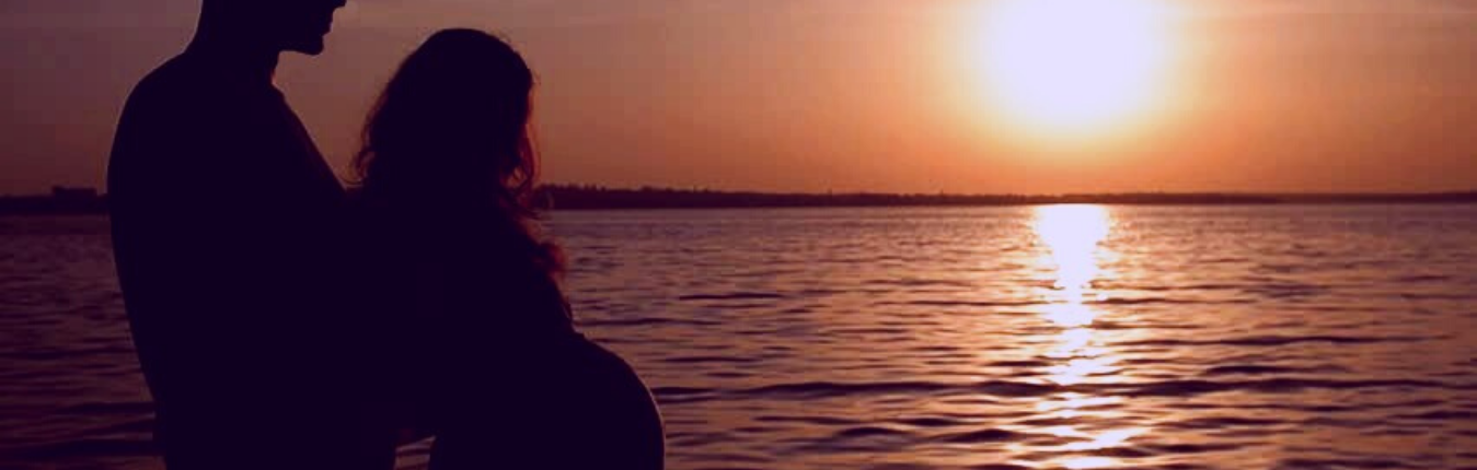 A man and pregnant wife watching the sunset on water