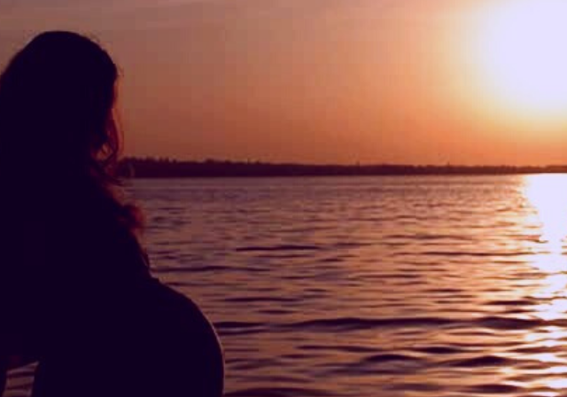 A man and pregnant wife watching the sunset on water