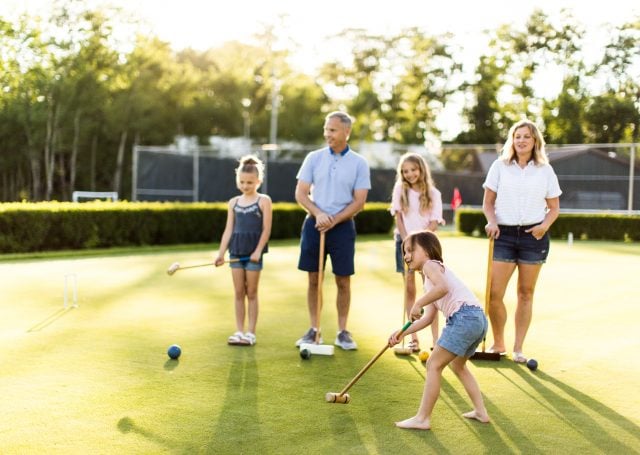 A group of girls playing croquet as their parents watch on