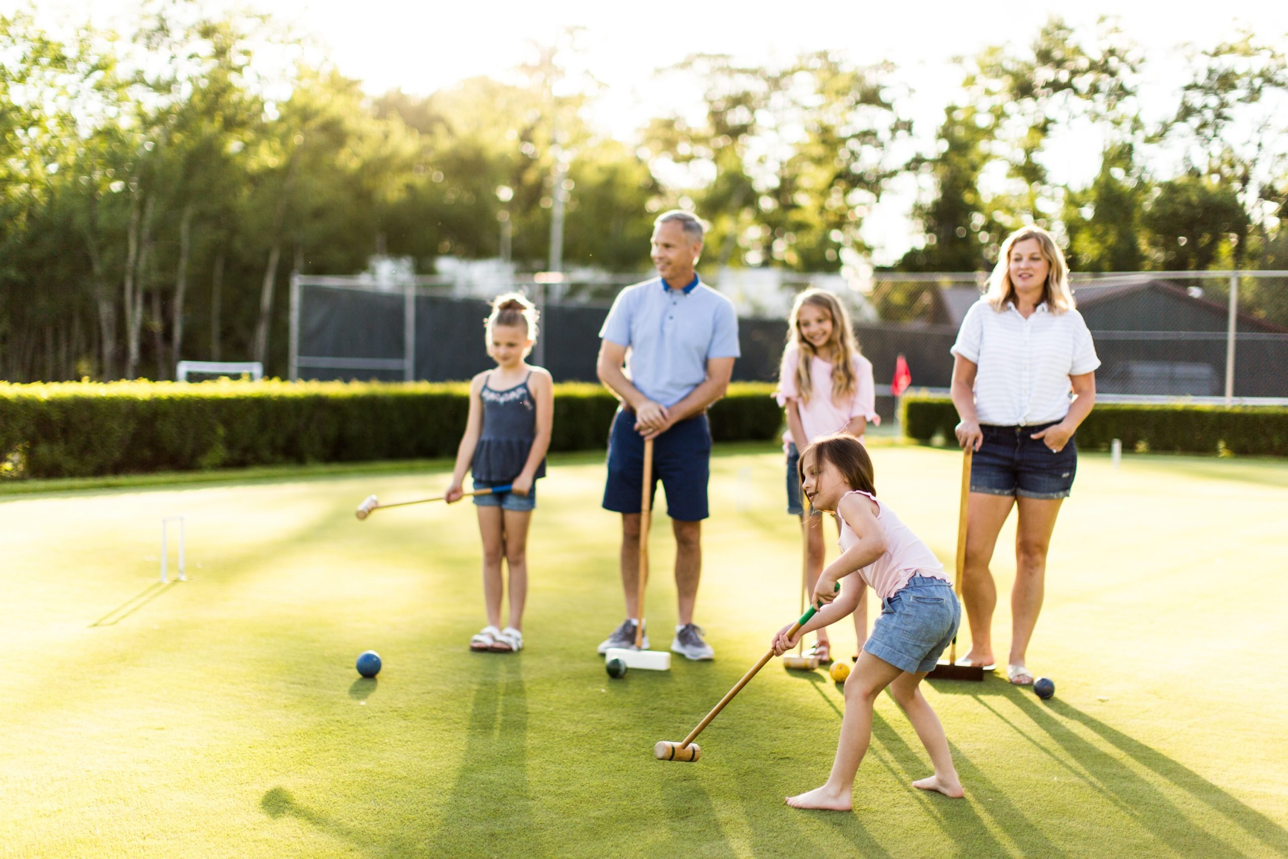 A group of girls playing croquet as their parents watch on