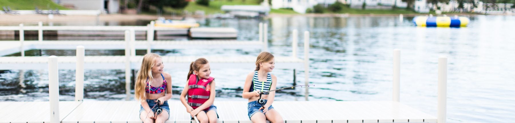 Three girls sitting on the dock with their legs dipped into the water and fishing