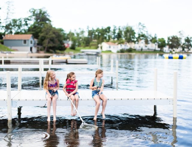 Three girls sitting on the dock with their legs dipped into the water and fishing