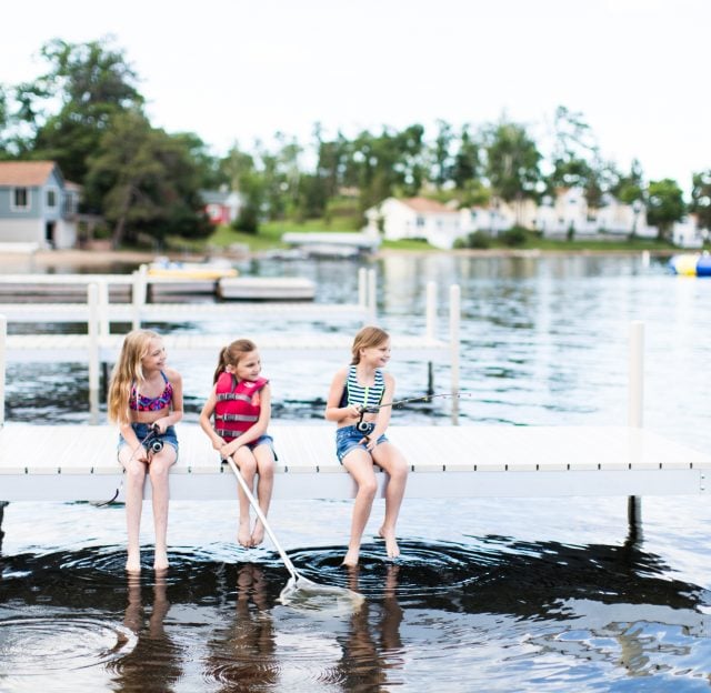 Three girls sitting on the dock with their legs dipped into the water and fishing