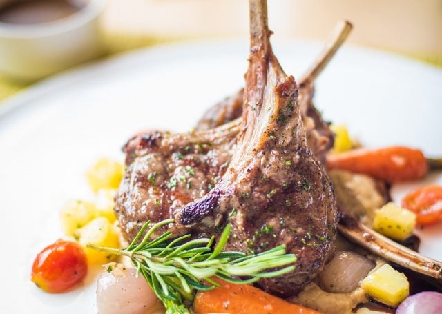 Lamb chop served with potatoes, carrots, onion, tomatoes, and garnished with rosemary leaves