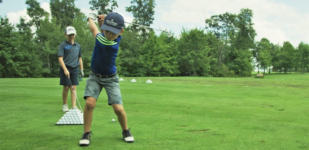 A boy swinging golf club as another boy looks on