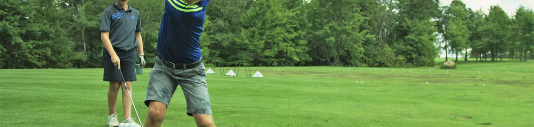 A boy swinging golf club as another boy looks on