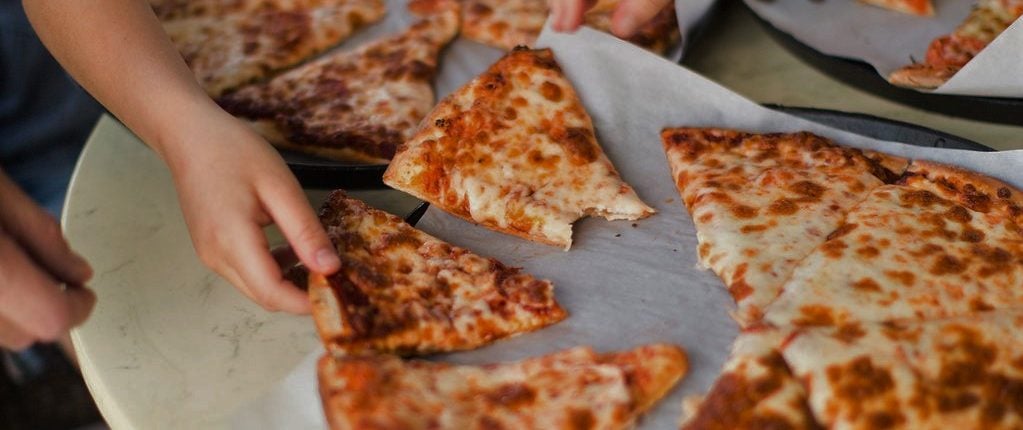 Hands placing half-eaten pizza slices next to pizzas