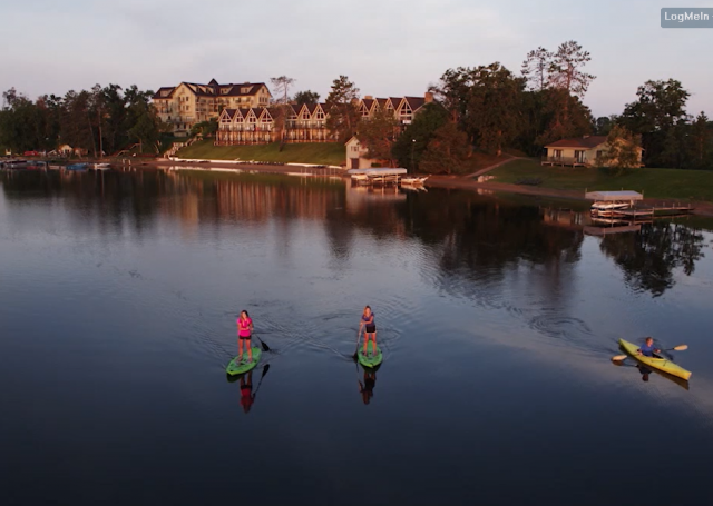 Two women paddleboarding next to a man kayaking on the Gull lake infront of the Madden's Resort building.