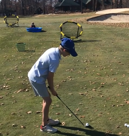 A boy swinging golf club to touch the ball