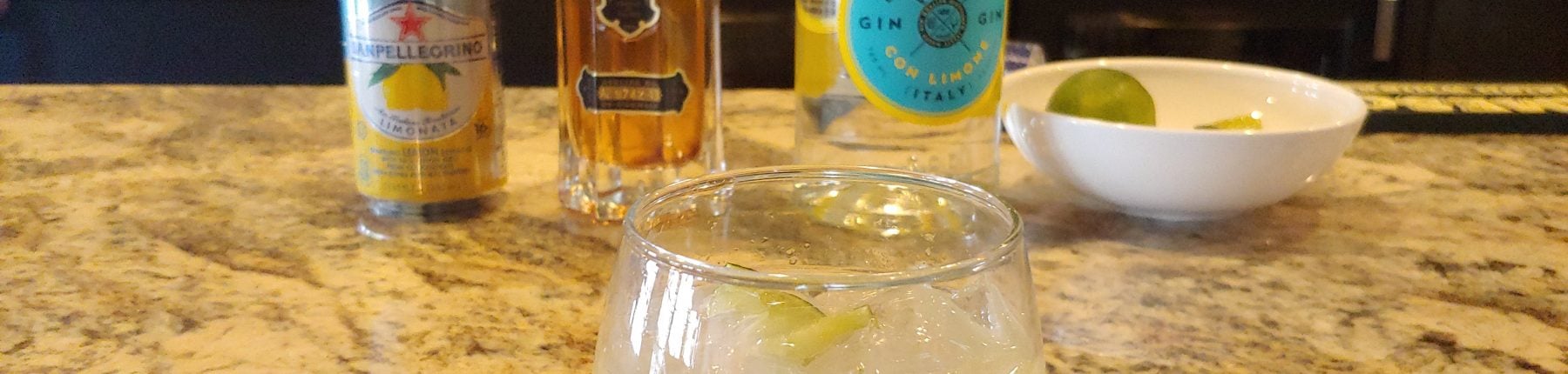 A cocktail placed in front of a can of lemonade, a St. Germain liquor bottle and a bottle of gin