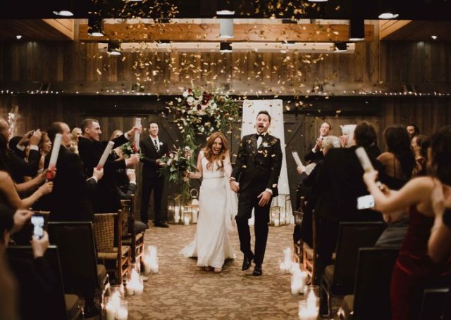 Bride and groom walking hand in hand as guests use confetti poppers on them