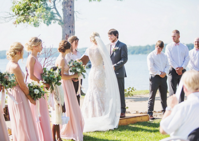 Bride and groom taking their vows in the outdoors next to their bridesmaids and groomsmen.