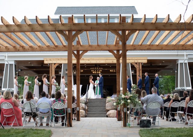Seated guests looking at the bride and groom taking their vows next to the bridesmaids and groomsmen at The Pavilion