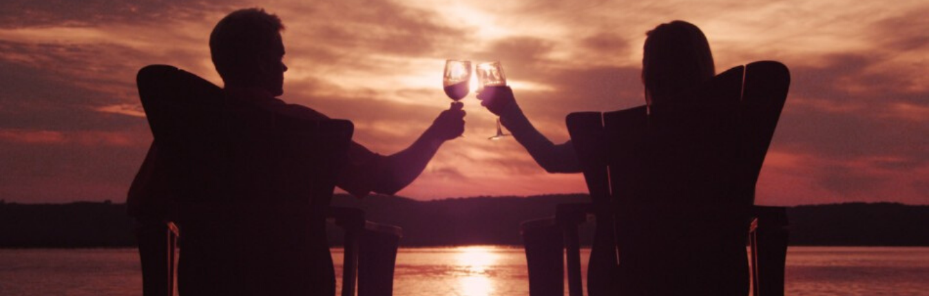 A couple clinking their wine glasses to cheers to the sunset by the water.