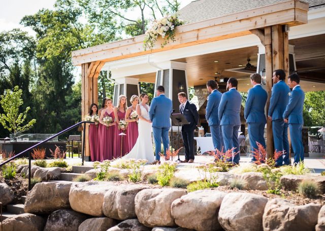 Bride and groom taking their vows in the outdoors next to their bridesmaids and groomsmen.