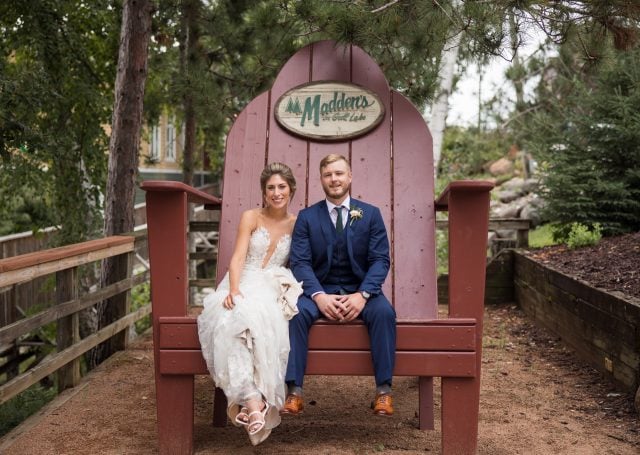 Bride and Groom sitting on a large wooden patio chair near The Pavilion building.