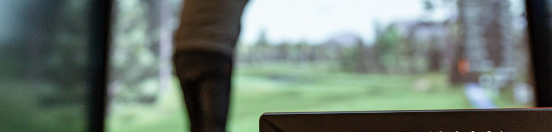 Rear view of a man swinging the golf club next to the Trackman dual radar