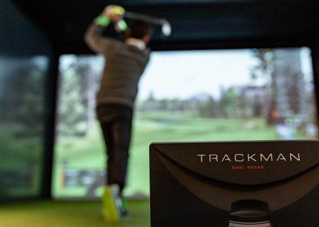 Rear view of a man swinging the golf club next to the Trackman dual radar