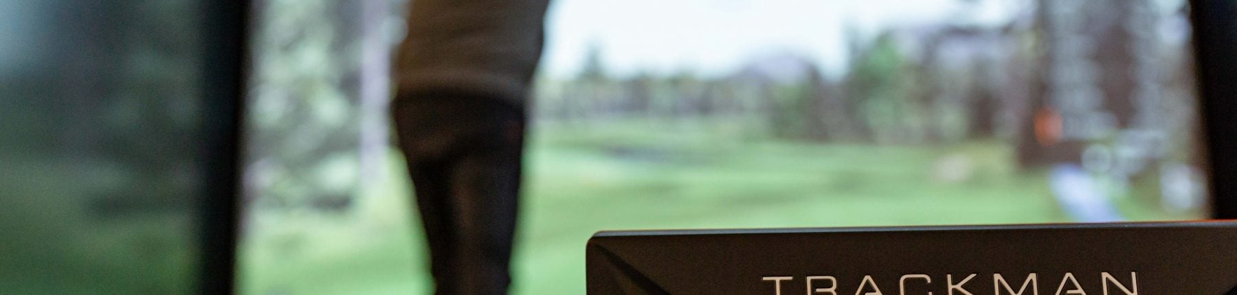 Rear view of a man swinging the golf club next to the Trackman dual radar