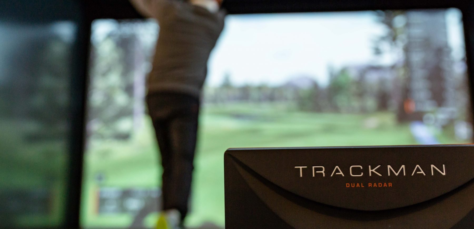 Rear view of a man swinging the golf club next to the Trackman dual radar
