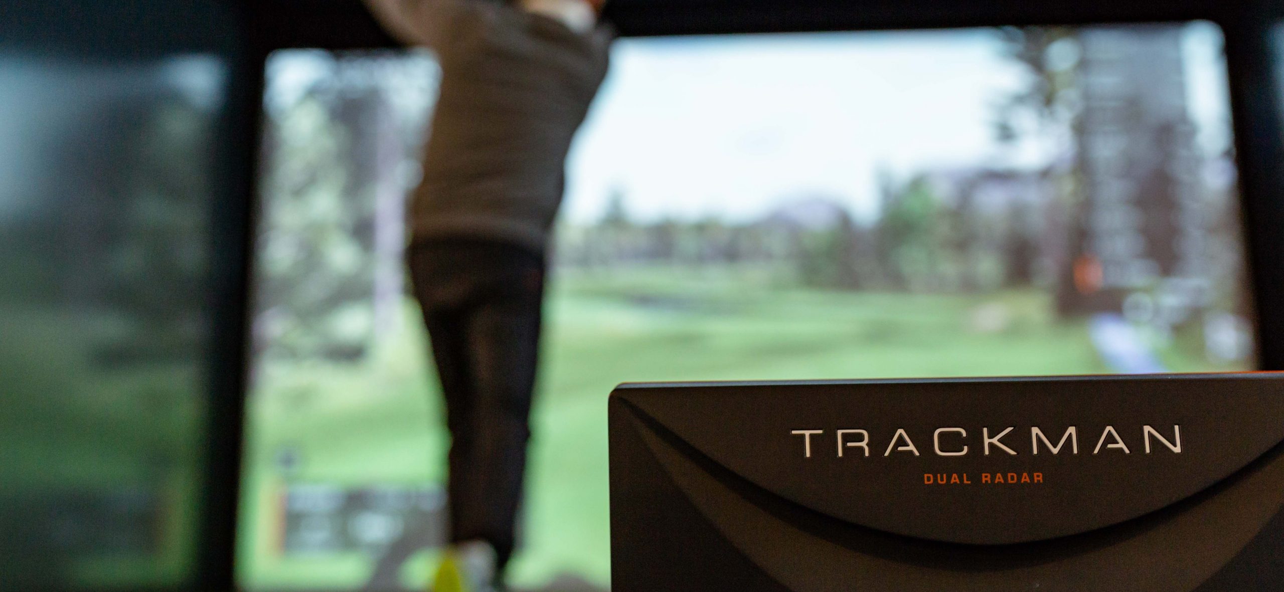 Rear view of a man swinging the golf club next to the Trackman dual radar