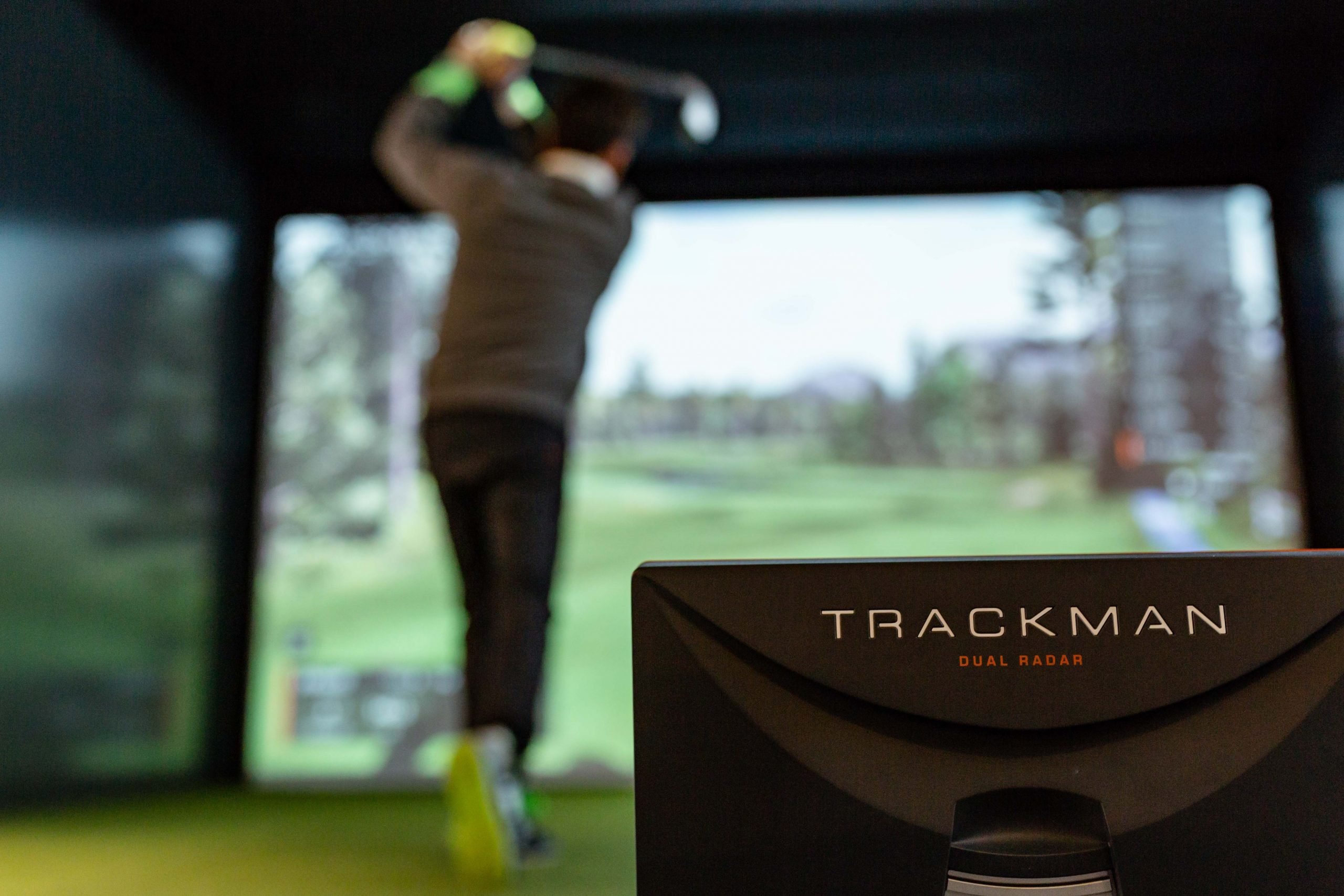 Rear view of a man swinging the golf club next to the Trackman dual radar