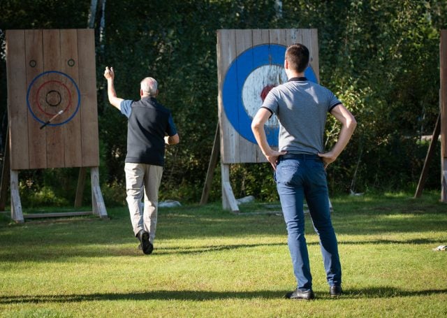 An elderly man throwing dart into the board as another watches on.