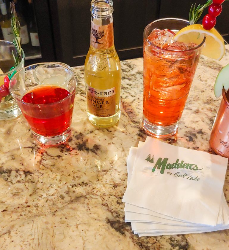 Cocktails next to a bottle of ginger ale placed on a marble counter with Madden's napkins