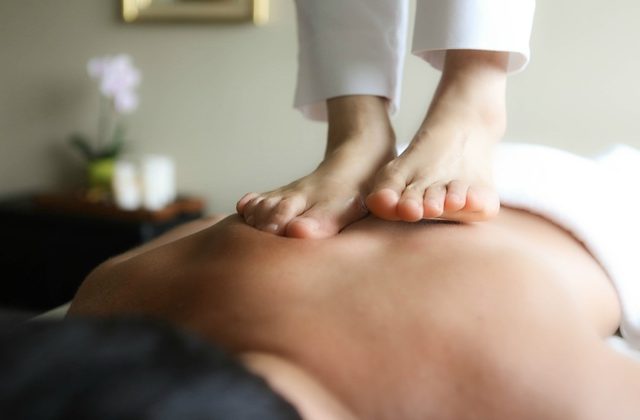 A man lying on his front and receiving ashiatsu massage from the therapist's feet