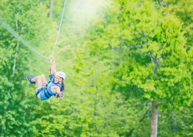 person swings on zip line over trees