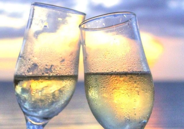 two champagne glasses clink by sunset