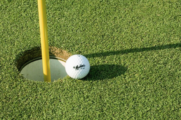 golf ball rests just on the edge of a cup