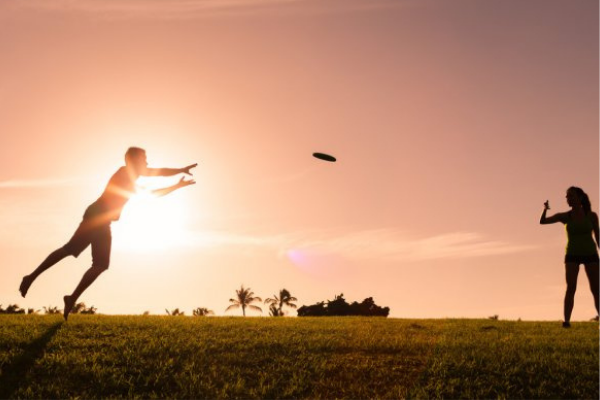 two people play frisbee at sunset