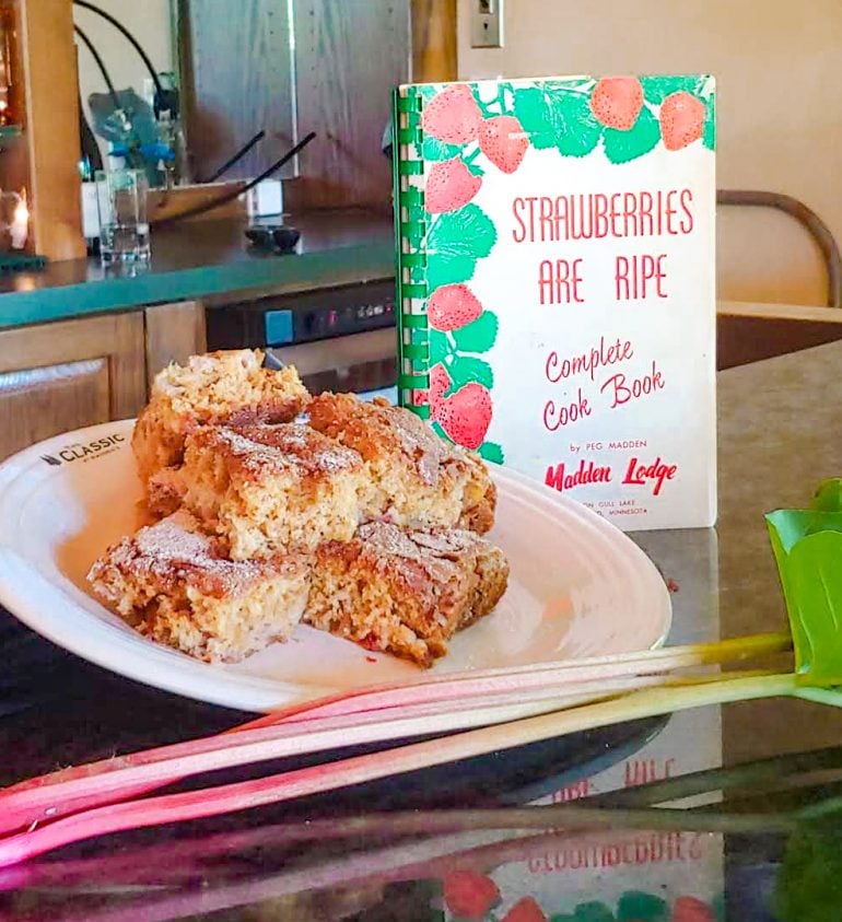 squares of rhubarb cake with fresh pieces of rhubarb and a cookbook