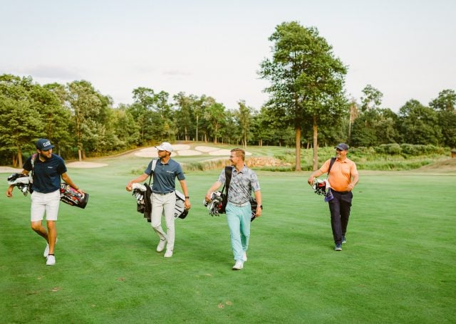 four golfers carrying their clubs walk off golf course