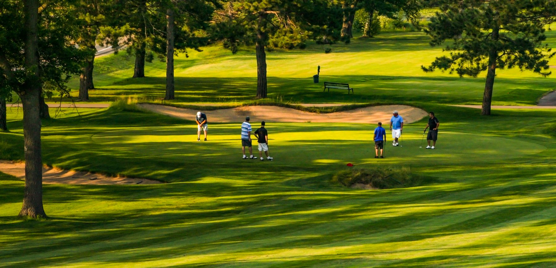 a group of golfers watch a play take a putt
