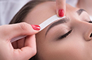 A therapist's hand waxing a woman's eyebrows